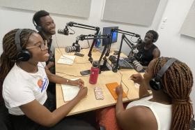 Group of young multicultural youth sitting in the podcast studio at Moe Library, talking into microphones.